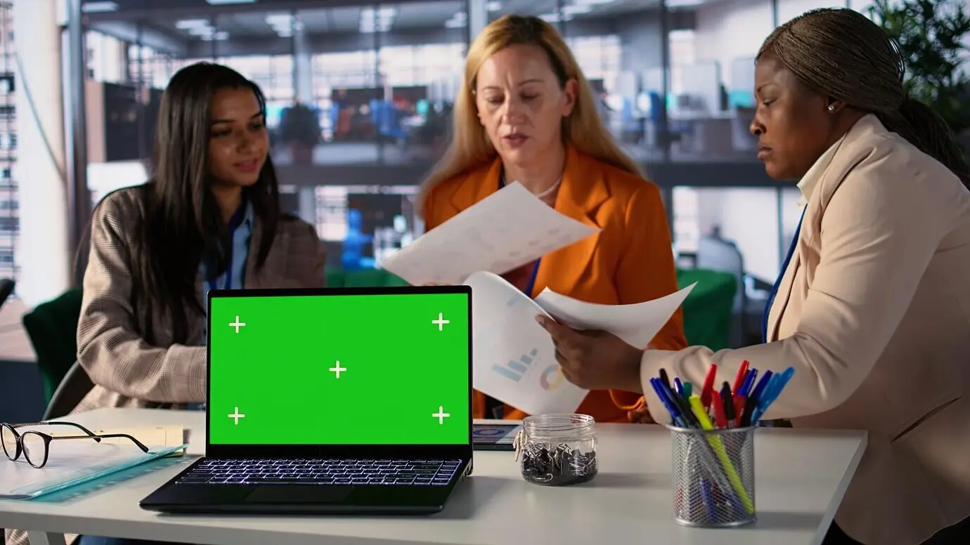 Деловые женщины разных национальностей работают рядом с изолированным зеленым экраном.